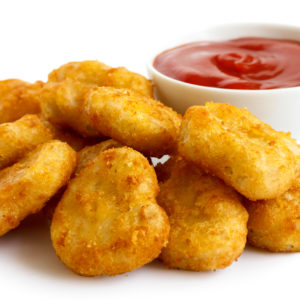 Pile of golden deep-fried battered chicken nuggets with bowl of ketchup, isolated on white.
